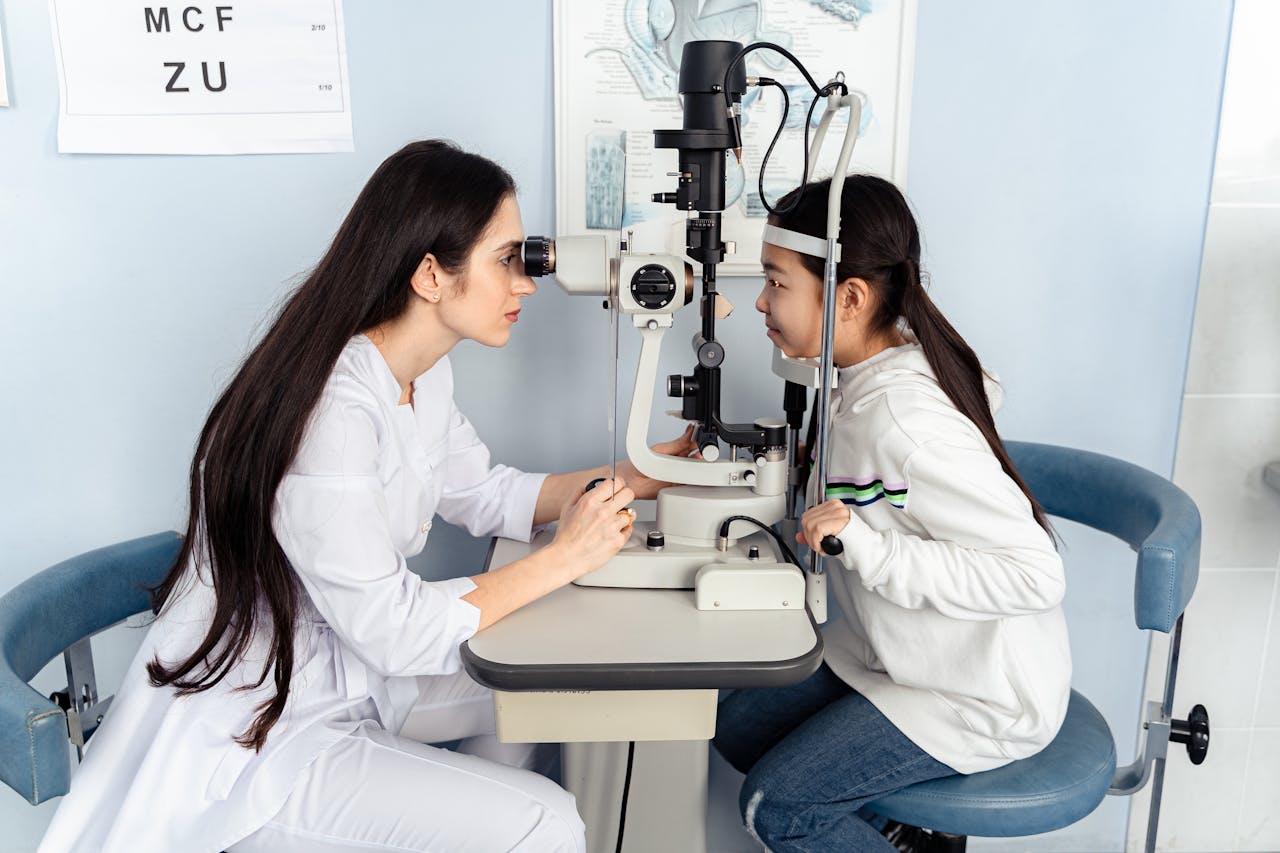 Optometrist performing vision test on child using medical equipment indoors.